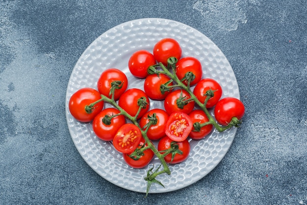 Pomodori ciliegia su un ramo su un tavolo di pietra scura piatto.