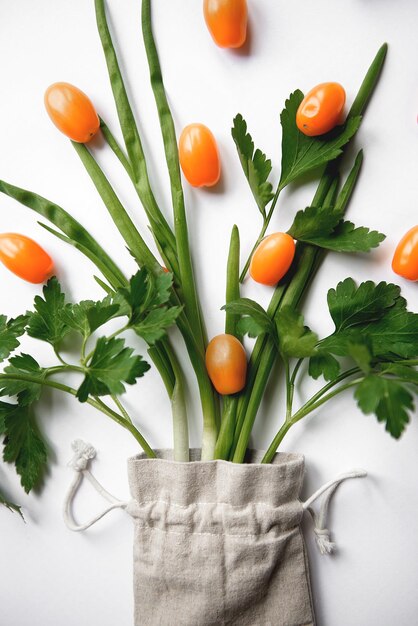 Pomodori ciliegini arancioni piatti con prezzemolo in un sacchetto di stoffa su sfondo bianco