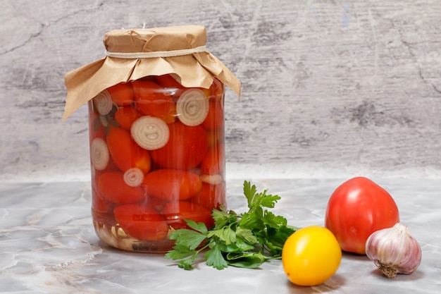 Pomodori conservati in un barattolo di vetro e pomodori freschi, foglie di prezzemolo, aglio sul tavolo della cucina.