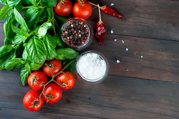 Pomodori e grappolo di basilico fresco verde su uno sfondo di legno scuro,