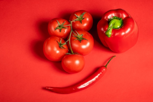 Pomodori e peperoncini rossi succosi delle verdure e peperoni dolci su una superficie rossa brillante