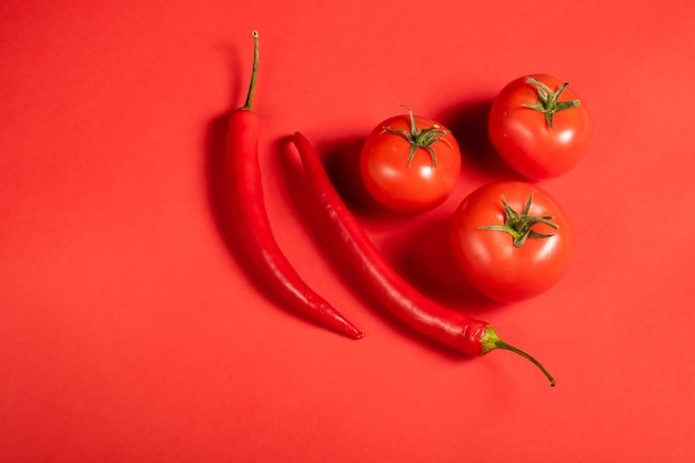 Pomodori e peperoncini rossi succosi delle verdure su una superficie rossa brillante