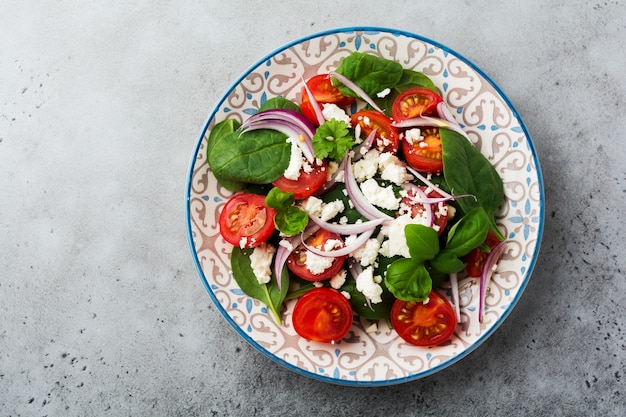 Pomodori, foglie di spinaci, cipolle rosse e insalata di formaggio feta su piatto in ceramica leggera su backround grigio