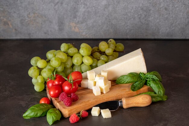 pomodori, formaggio, basilico, lamponi e uva su un tagliere di olive su sfondo scuro