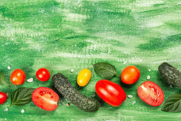 Pomodori freschi, cetrioli e foglie di basilico. Verdure mature su un fondo di legno verde. Ingredienti utili per cibo sano, vista dall'alto