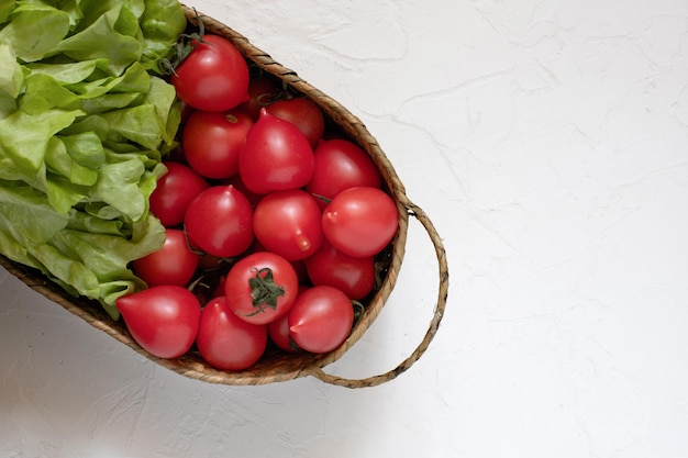 Pomodori freschi e foglie di lattuga in un cesto di vimini su una superficie bianca Harvest Farm product
