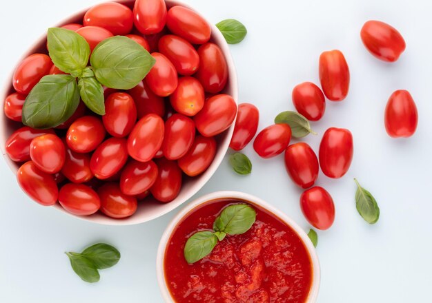 Pomodori freschi in ciotola sulla tavola pastello. Sfondo di pomodoro, verdure sane e foglie di basilico.