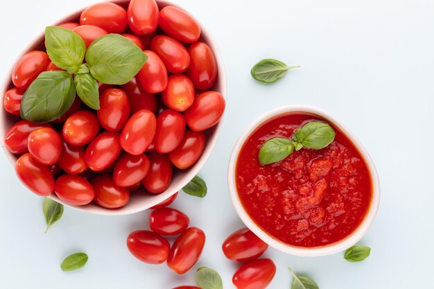 Pomodori freschi in una ciotola sul tavolo pastello. Sfondo di pomodoro, verdure sane e foglie di basilico.