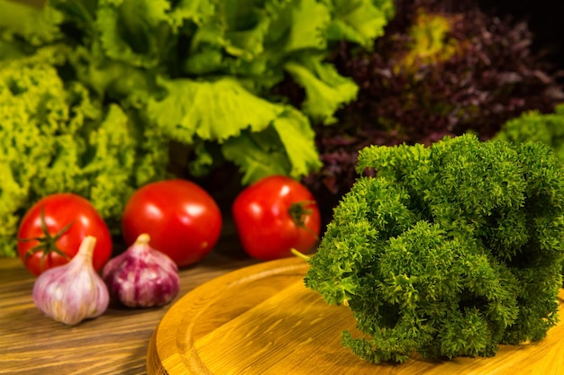 Pomodori freschi maturi e bulbi d'aglio su un tavolo di legno con un'insalata verde sullo sfondo Delizioso cibo vegetariano