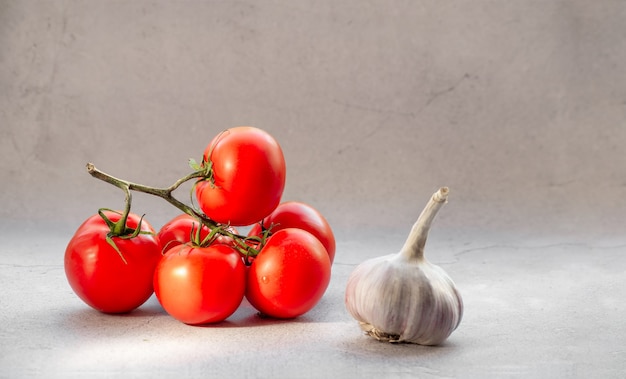 Pomodori freschi su una vite con aglio su sfondo chiaro.