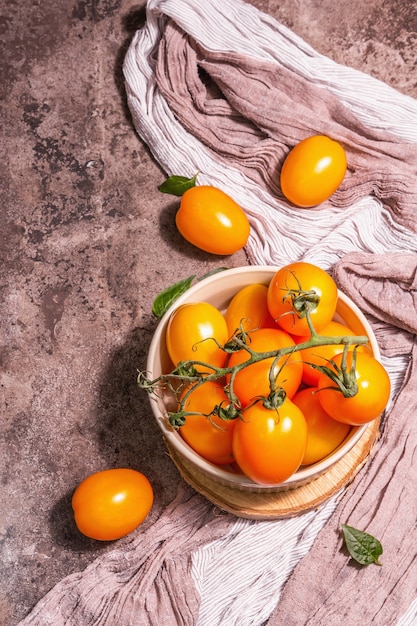 Pomodori giallo-arancio in una ciotola di ceramica. Verdure fresche mature, prodotto biologico dell'agricoltore. Una luce dura alla moda, un'ombra scura, un supporto in legno, uno sfondo in pietra di marmo, vista dall'alto