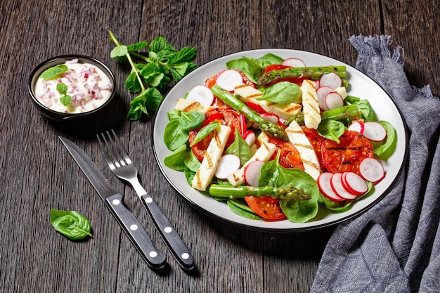 pomodori grigliati, formaggio Halloumi, asparagi, ravanelli e insalata di spinaci su un piatto su un tavolo di legno con salsa di maionese in una ciotola, vista orizzontale dall'alto