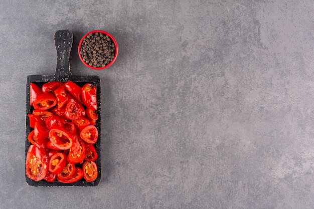 Pomodori in salamoia con pepe in grani posti su un tavolo di pietra.