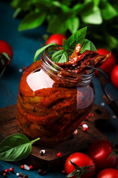 Pomodori italiani essiccati al sole in olio d'oliva con basilico verde e spezie in barattolo di vetro sullo spazio blu della copia del tavolo da cucina