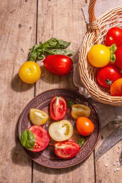 Pomodori maturi assortiti con basilico fresco. Nuove verdure del raccolto in un canestro di vimini. Vecchio fondo in legno, vista dall'alto