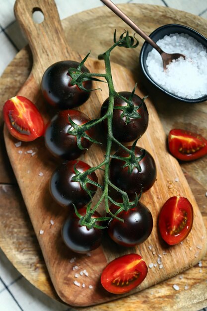 Pomodori neri su un ramo su una tavola di legno con sale marino