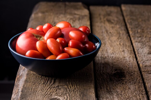 Pomodori piccoli e grandi rossi sulla piastra blu su sfondo di legno Spazio di copia vegetale biologico