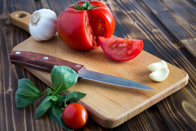 Pomodori rossi aglio e coltello da cucina sul tagliere marrone