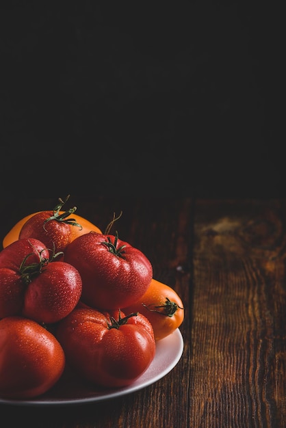 Pomodori rossi e gialli freschi sul piatto bianco sopra la superficie di legno