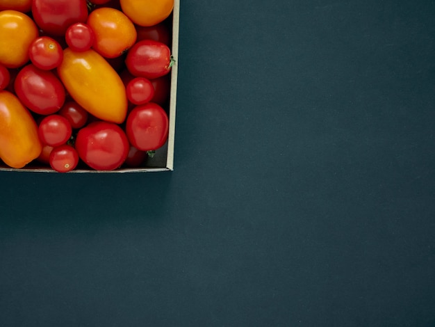 Pomodori rossi e gialli in una scatola di cartone su uno sfondo scuro con spazio di copia