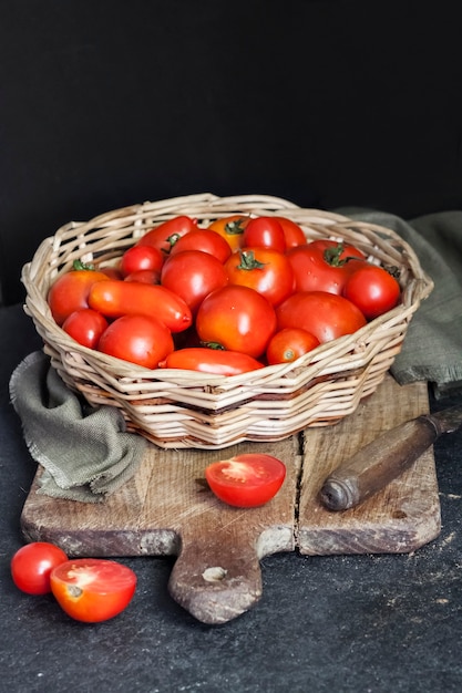 Pomodori rossi freschi in cesto di vimini su sfondo nero.