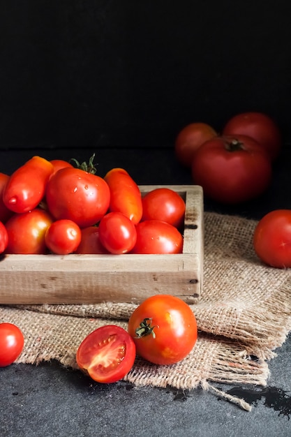 Pomodori rossi freschi in scatola di legno su sfondo nero. Copia spazio