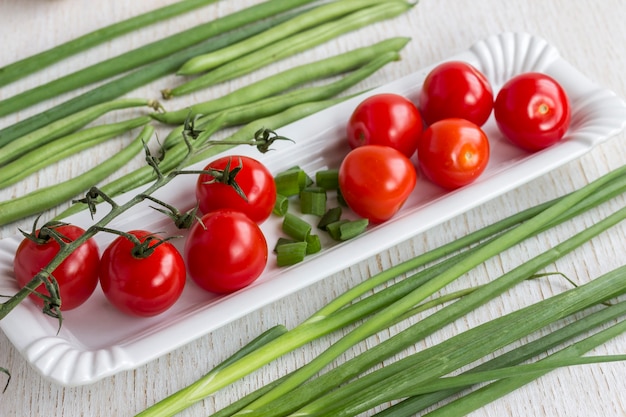 Pomodori rossi in un piatto bianco. Cipolle e asparagi su bianco