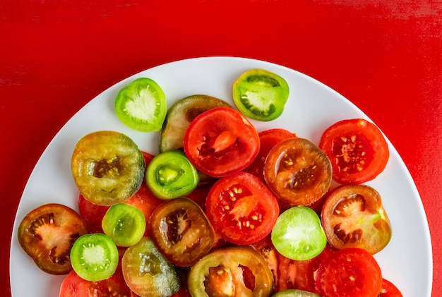 Pomodori rossi, verdi e kumato affettati sul piatto bianco su fondo di legno rosso