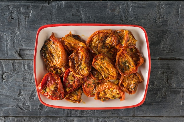 Pomodori secchi con aglio e pepe in olio d'oliva in un piatto su un tavolo di legno. Antipasto di pomodoro mediterraneo. Cibo vegetariano. La vista dall'alto.