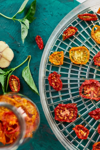 Pomodori secchi fatti in casa con erbe aromatiche, sul setaccio dall'essiccatore su sfondo verde. Vista dall'alto, copia spazio, laici piatta