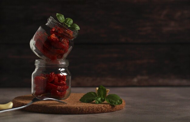 Pomodori secchi in un barattolo di vetro con aglio e basilico con una forchetta su sfondo scuro