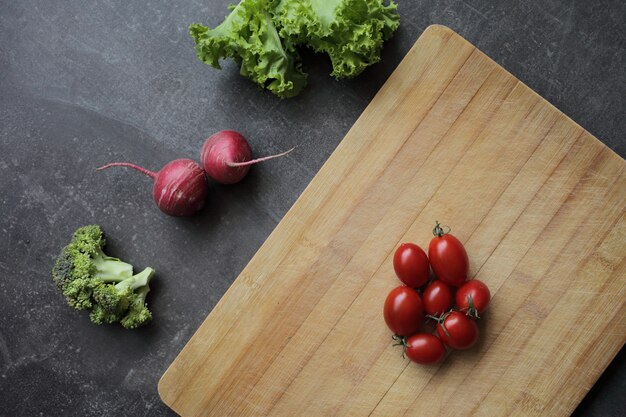 Pomodori su un tagliere su un tavolo grigio e verdure fresche