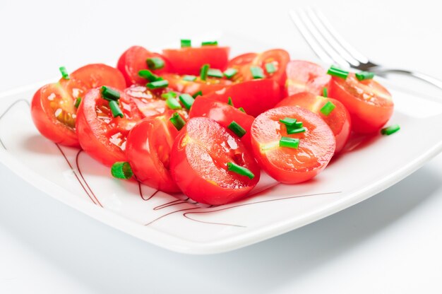 Pomodorini decorati con cipolle verdi. Su un piatto quadrato bianco.