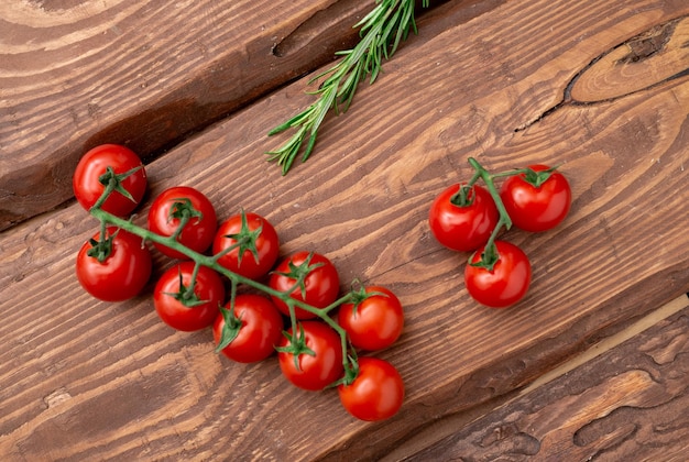 Pomodorini e rosmarino su uno sfondo di legno Ramo di pomodoro fresco Cibo vegetariano