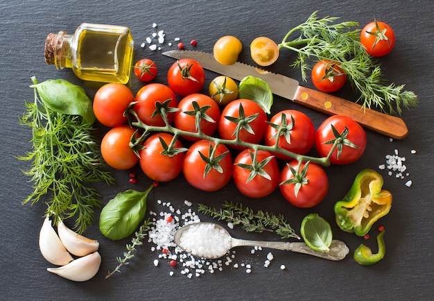 Pomodorini, erbe aromatiche e olio d'oliva su una tavola scura