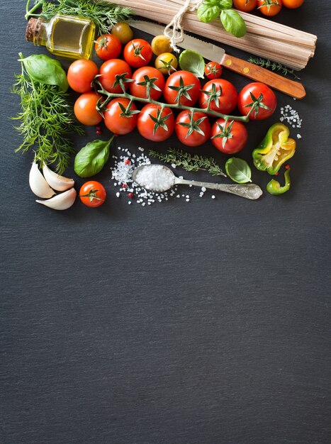 Pomodorini, erbe aromatiche, pasta e olio d'oliva su un bordo scuro con spazio di copia