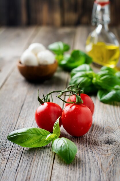 Pomodorini freschi, foglie di basilico, mozzarella e olio d'oliva su una vecchia superficie in legno. Ingredienti per insalata caprese. Messa a fuoco selettiva.