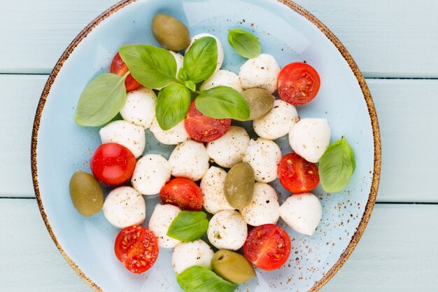 Pomodorini, mozzarella, basilico e spezie sulla lavagna di pietra grigia ardesia. Ingredienti dell'insalata caprese tradizionale italiana. Cucina mediterranea.