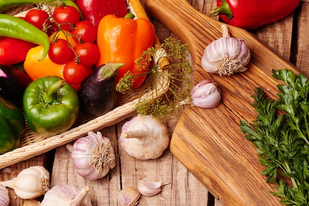 Pomodorini, peperoni, aglio, melanzane in un cesto di vimini. Verdure fresche su un tavolo di legno.