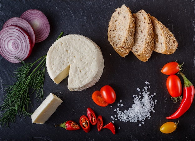 Pomodorini rossi e gialli su ardesia con fette di pane, cipolla, formaggio a pasta molle e sale