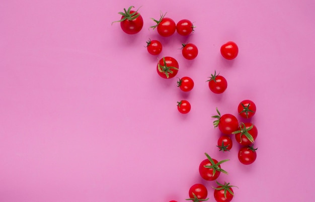 Pomodorini rossi freschi su sfondo rosa. Era disteso. Vista dall'alto di un pomodoro succoso maturo su uno sfondo rosa. Carta da parati con pomodori. Trama vegetale. Un luogo da copiare.