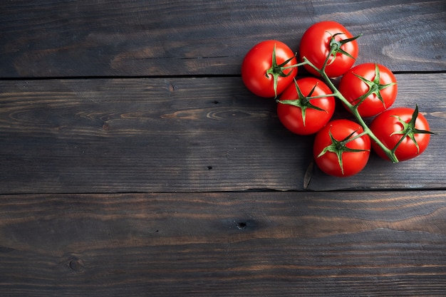 Pomodorini su un ramo. Pomodori rossi succosi freschi su un fondo di legno scuro. .