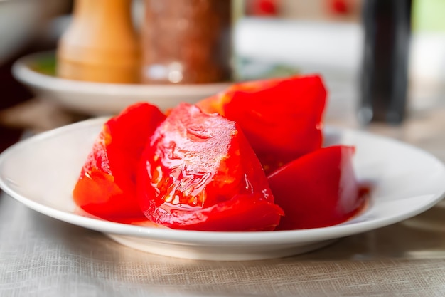 Pomodoro a fette Primo piano succose fette di pomodoro maturo impilate in un piatto bianco sul tavolo della cucina