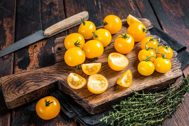 Pomodoro ciliegino giallo a fette su un tagliere di legno. Tavolo in legno scuro. Vista dall'alto.