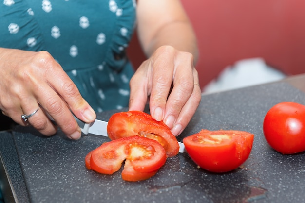 Pomodoro di taglio della donna con il coltello, sul piatto