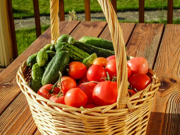 Pomodoro e cetriolo freschi in un canestro, sulla vecchia tavola di legno, estate all&#39;aperto.