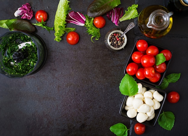 Pomodoro e mozzarella dell'insalata di Caprese degli ingredienti con basilico e le erbe sul nero.