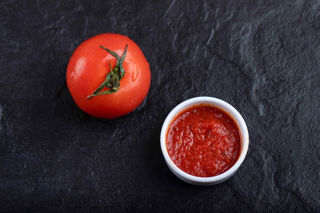 Pomodoro fresco rosso con salsa posto su uno sfondo nero.