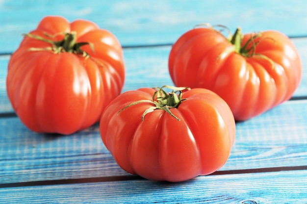 Pomodoro maturo rosso tre con il gambo verde su una priorità bassa blu