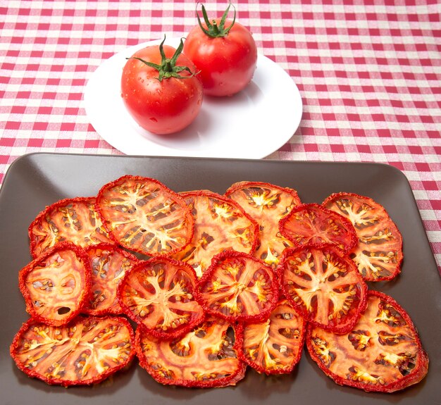 Pomodoro rosso fresco e fette di pomodoro secco su un piatto. Alimento vegetale vitaminico